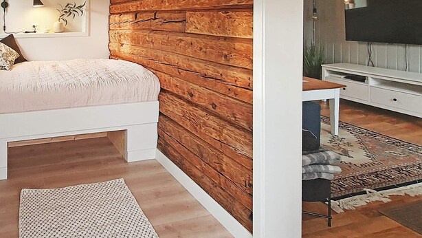 A bedroom with a wooden accent wall, a bed, a desk, and a television. - 4 Star Holiday Home in Bud (Hustadvika)