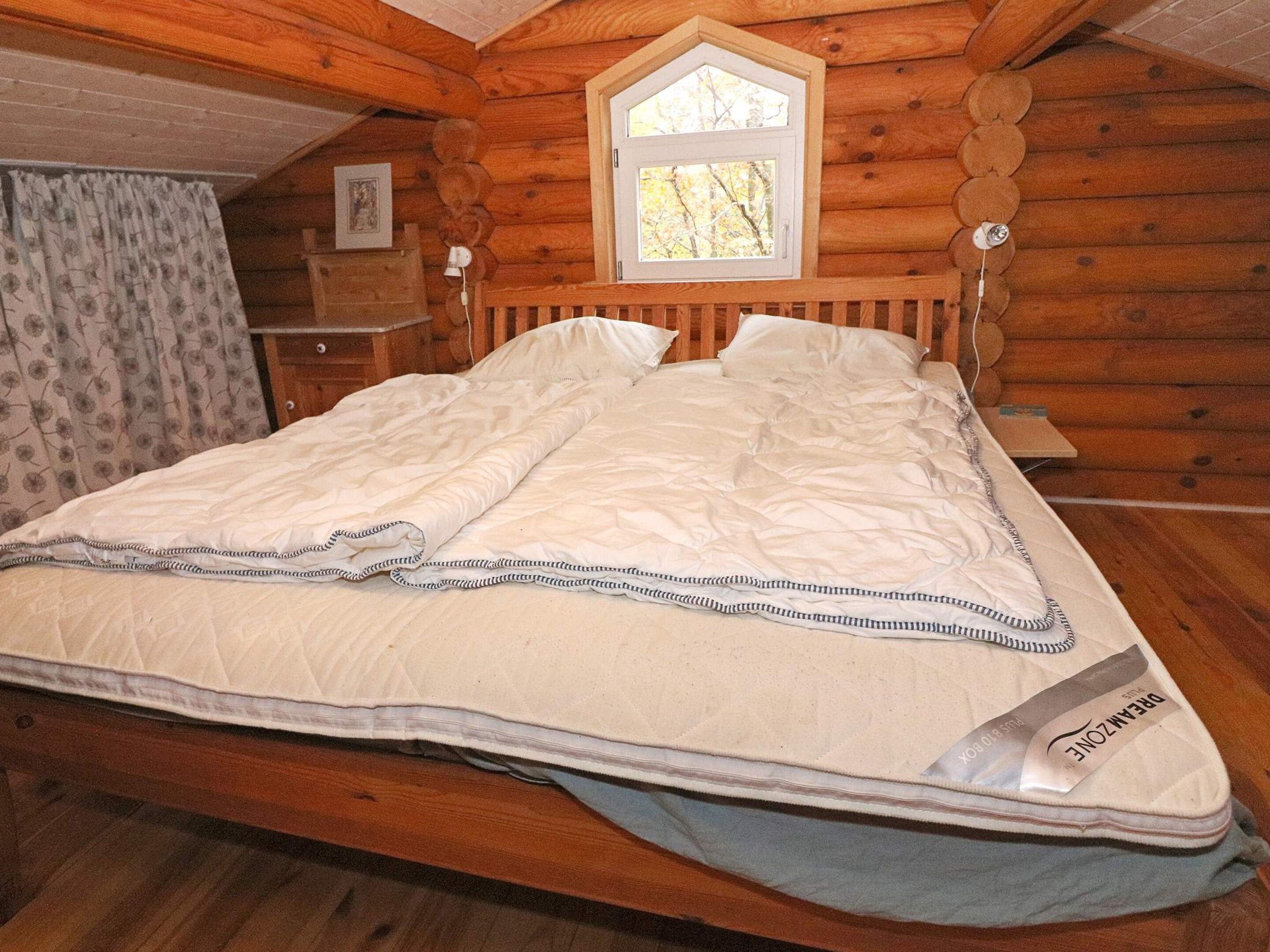 A wooden cabin bedroom with a bed, a window, and a nightstand.