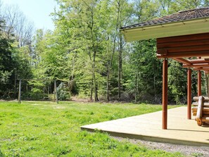 A wooden deck with a pergola structure, surrounded by a grassy area and dense trees. - 4 Star Holiday Home in Hadsund (Hadsund)