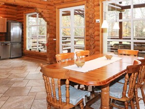 A wooden cabin interior with a dining table, chairs, a refrigerator, and large windows. - 4 Star Holiday Home in Hadsund (Hadsund)