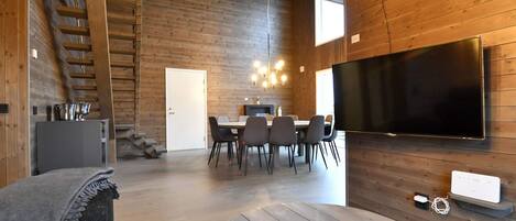Un intérieur moderne comprenant un coin repas, un téléviseur à écran plat fixé au mur et un escalier menant à un niveau supérieur.