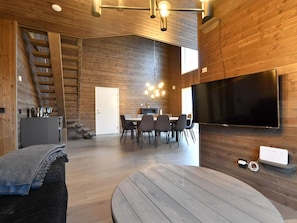 Un interior moderno con zona de comedor, televisor de pantalla plana montado en la pared y una escalera que conduce a un nivel superior.