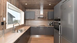 Une cuisine moderne avec un plafond en bois, des appareils électroménagers en acier inoxydable et une fenêtre donnant sur un immeuble.