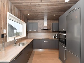 Une cuisine moderne avec un plafond en bois, des appareils électroménagers en acier inoxydable et une fenêtre donnant sur un immeuble.