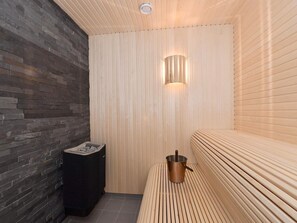 Una sala de sauna con un banco de madera, un calentador en la pared y un calentador negro en el suelo.