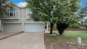 A two-story house with a garage, a driveway, and a tree in the front yard.