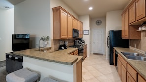 A modern kitchen with wooden cabinets, a granite countertop, a black refrigerator, and a coffee station.