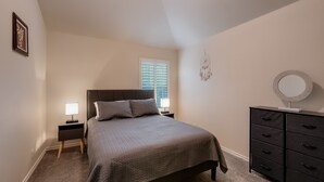 A bedroom with a bed, nightstands, a dresser, and a window with blinds.