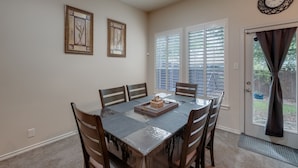 A dining room with a table set for four, framed artwork on the wall, and a door with a view to the outside.
