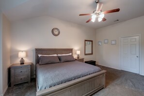 Une chambre à coucher avec un lit, des tables de chevet, un ventilateur de plafond, une horloge et une porte.