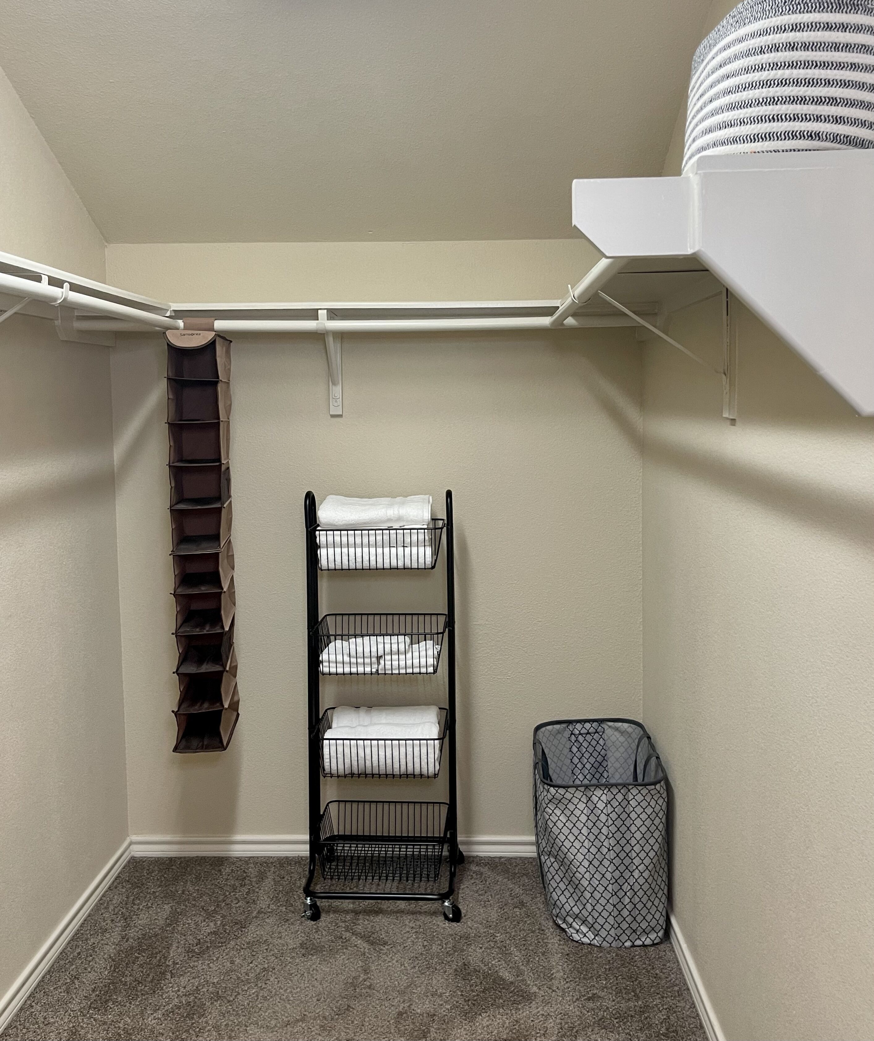 A storage closet with a metal rack holding folded towels, a hanging shoe rack, and a laundry basket.