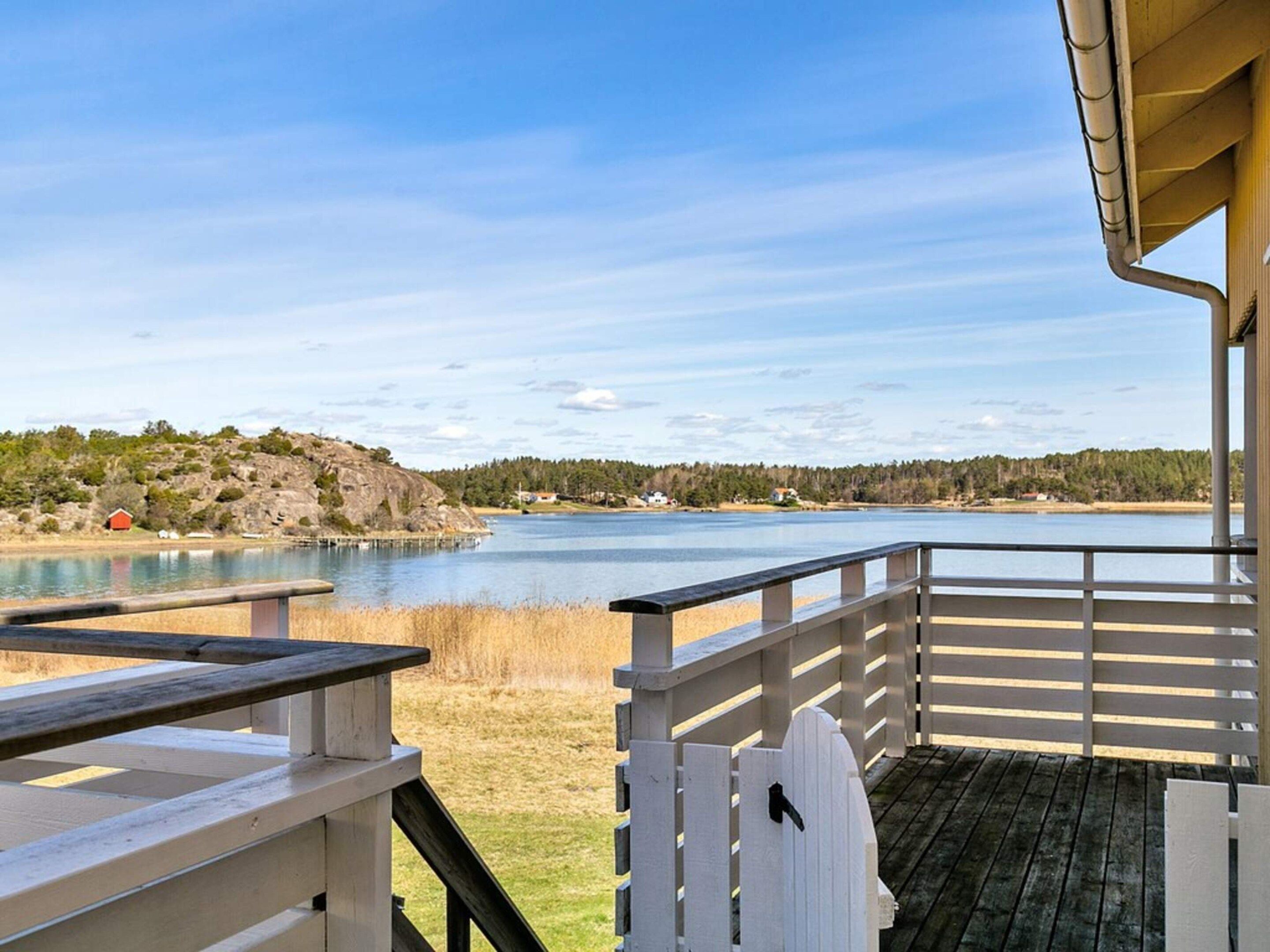 Une terrasse en bois avec une balustrade donnant sur un lac, avec des maisons et des arbres en arrière-plan.
