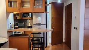 A compact kitchen with wooden cabinets, a stainless steel refrigerator, and a small bar area with stools.