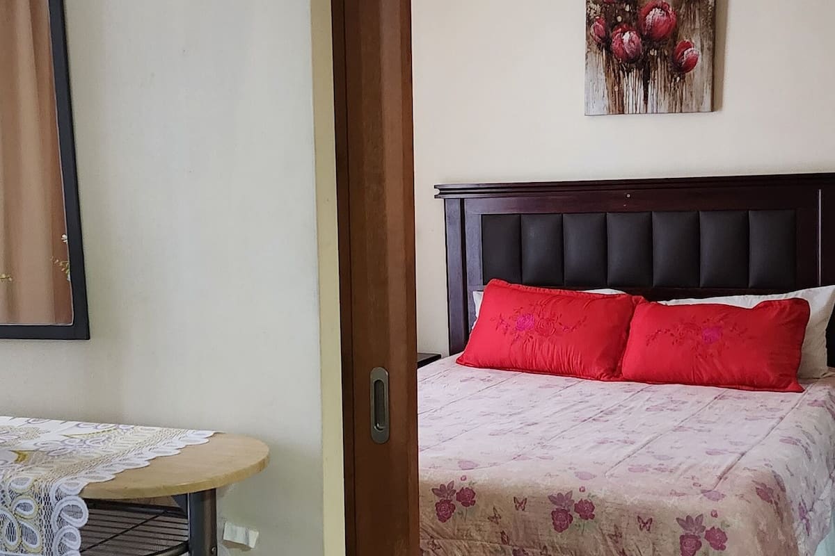 Un dormitorio con una cama, una mesita redonda con mantel de encaje y un cuadro en la pared.