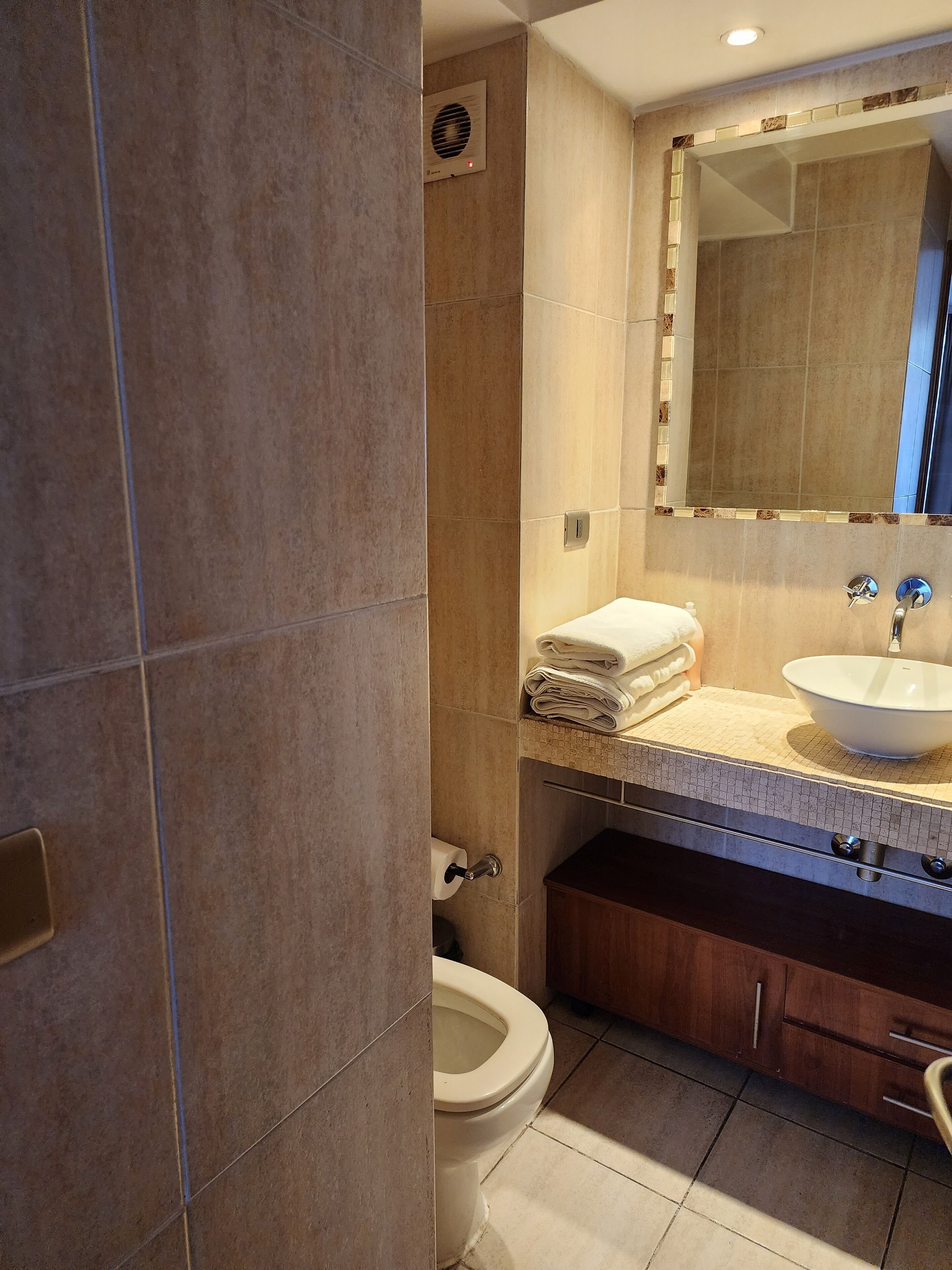 A modern bathroom with a beige tiled wall, a white sink, and a wooden cabinet.