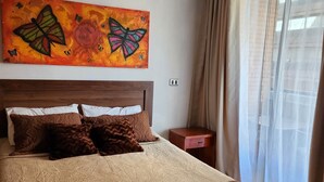 A bedroom with a large bed, a nightstand, a painting, and a window with curtains.