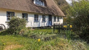 A traditional thatched-roof house with a white exterior, multiple windows, and a garden with daffodils. - 6 Person Holiday Home in Soby Aero (Soby)