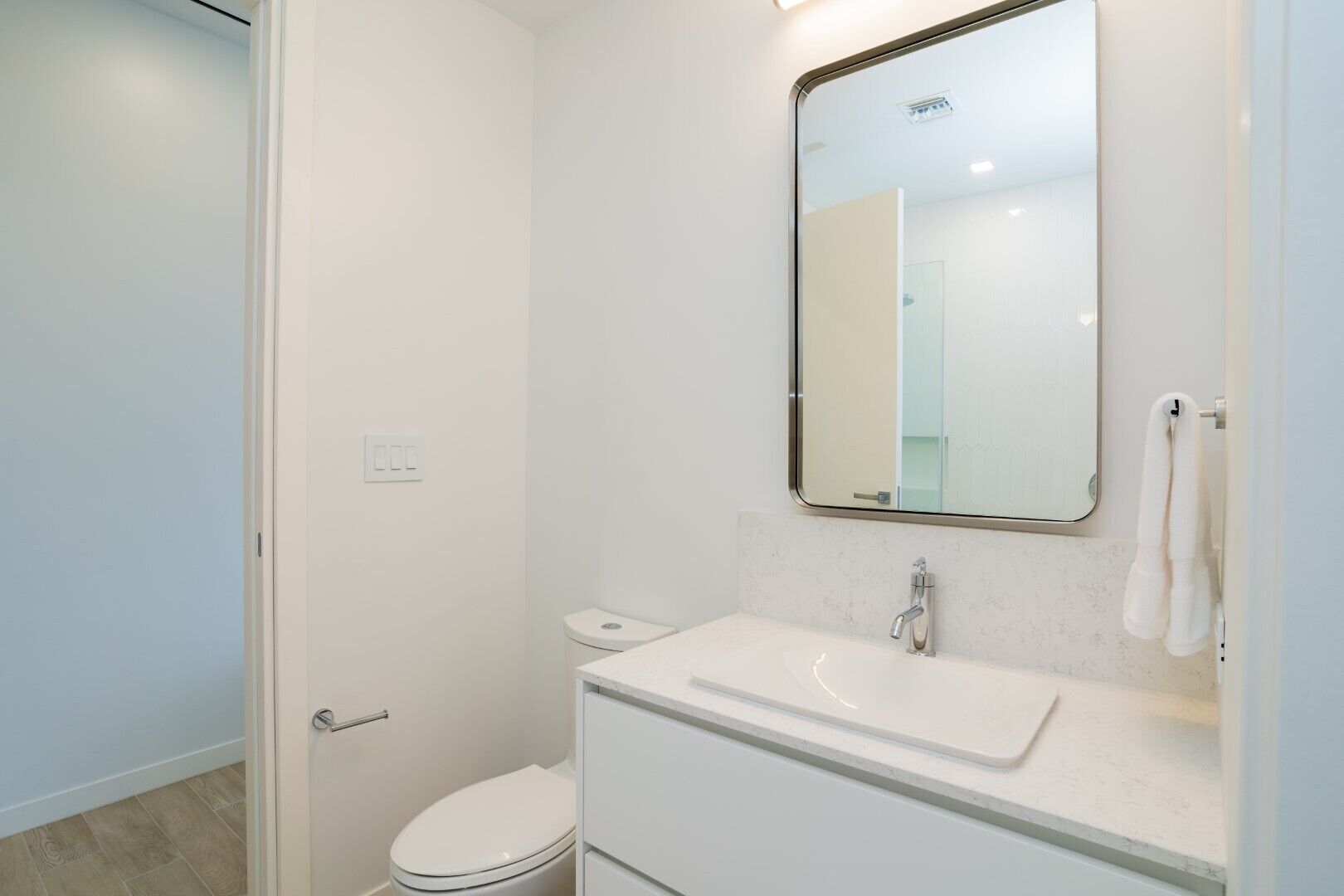 Een kleine, schone badkamer met een wit toilet, een wastafel met spiegel erboven en een handdoek aan de muur.