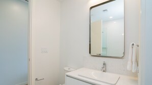 Une petite salle de bain propre, avec des toilettes blanches, un lavabo surmonté d’un miroir et une serviette accrochée au mur.