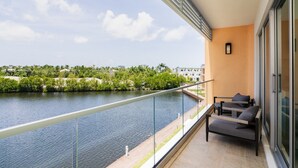 Un balcon donnant sur une rivière et sur un paysage verdoyant, avec une balustrade en verre et un espace détente agrémenté de coussins.