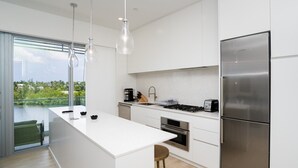 Une cuisine moderne dotée d’un grand îlot central, d’appareils électroménagers en acier inoxydable et offrant une vue sur un plan d’eau.