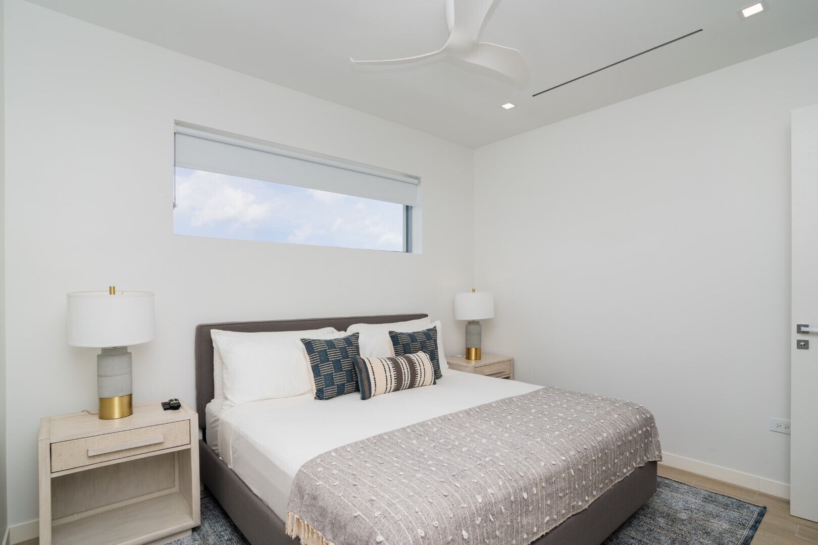 A modern bedroom with a large bed, two bedside tables, a window, and a ceiling fan.