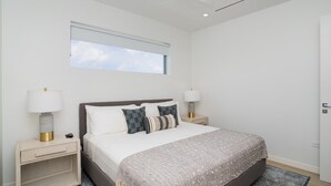 Une chambre moderne avec un grand lit, deux tables de chevet, une fenêtre et un ventilateur de plafond.