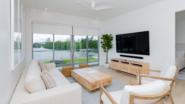 A modern living room with a large TV, comfortable seating, and a view of a body of water. - Luxury 2 Bed 2 Bath Premium Condo - (Grand Cayman)