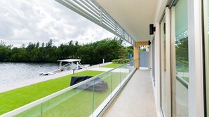 A balcony with a view of a water body, a grassy area, and a boat dock. - Luxury 2 Bed 2 Bath Premium Condo - (Grand Cayman)