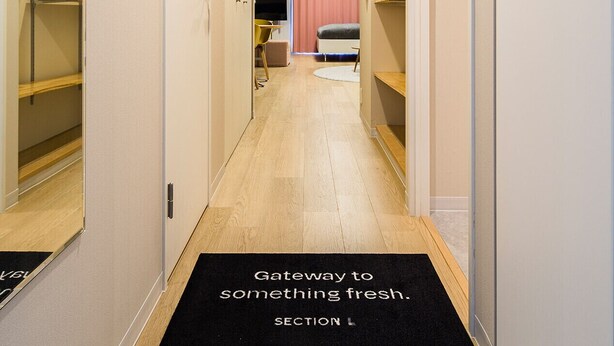 A hotel hallway with a black doormat, wooden flooring, and a bed in the background. - Section L Residence Ginza (Tokyo)