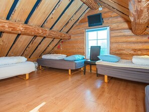 A cozy attic room with wooden beams, a television, and two beds with pillows.