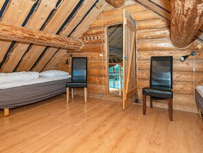 Ein Blockhauszimmer mit einem Bett, zwei Stühlen, einem Schreibtisch und einem Fenster.