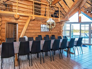 A wooden interior with a long table set for dining, a chandelier, and a large window.