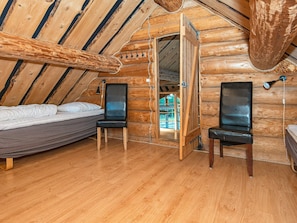 Habitació d'una cabana de fusta amb un llit, dues cadires, un escriptori i una finestra.