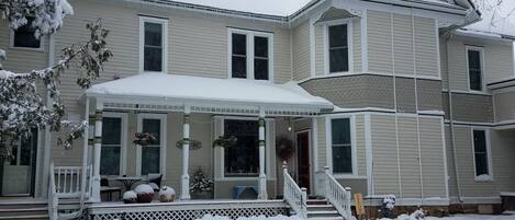 A two-story house with a covered porch and a snow-covered lawn.