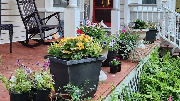 A porch with potted plants, a rocking chair, and a welcome sign. - Oaklawn Inn LLC (Menomonie)