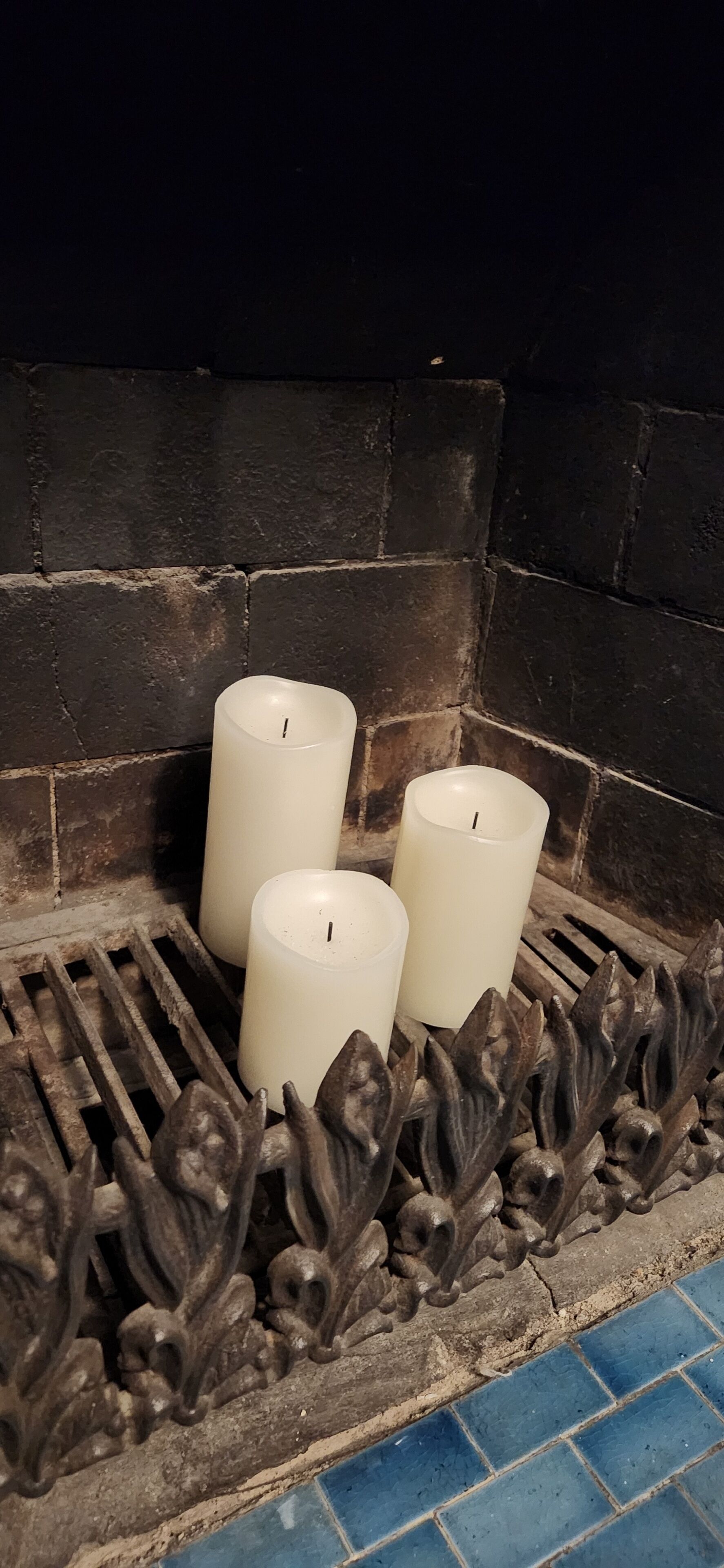 Three white candles placed on a metal grate in front of a stone wall.