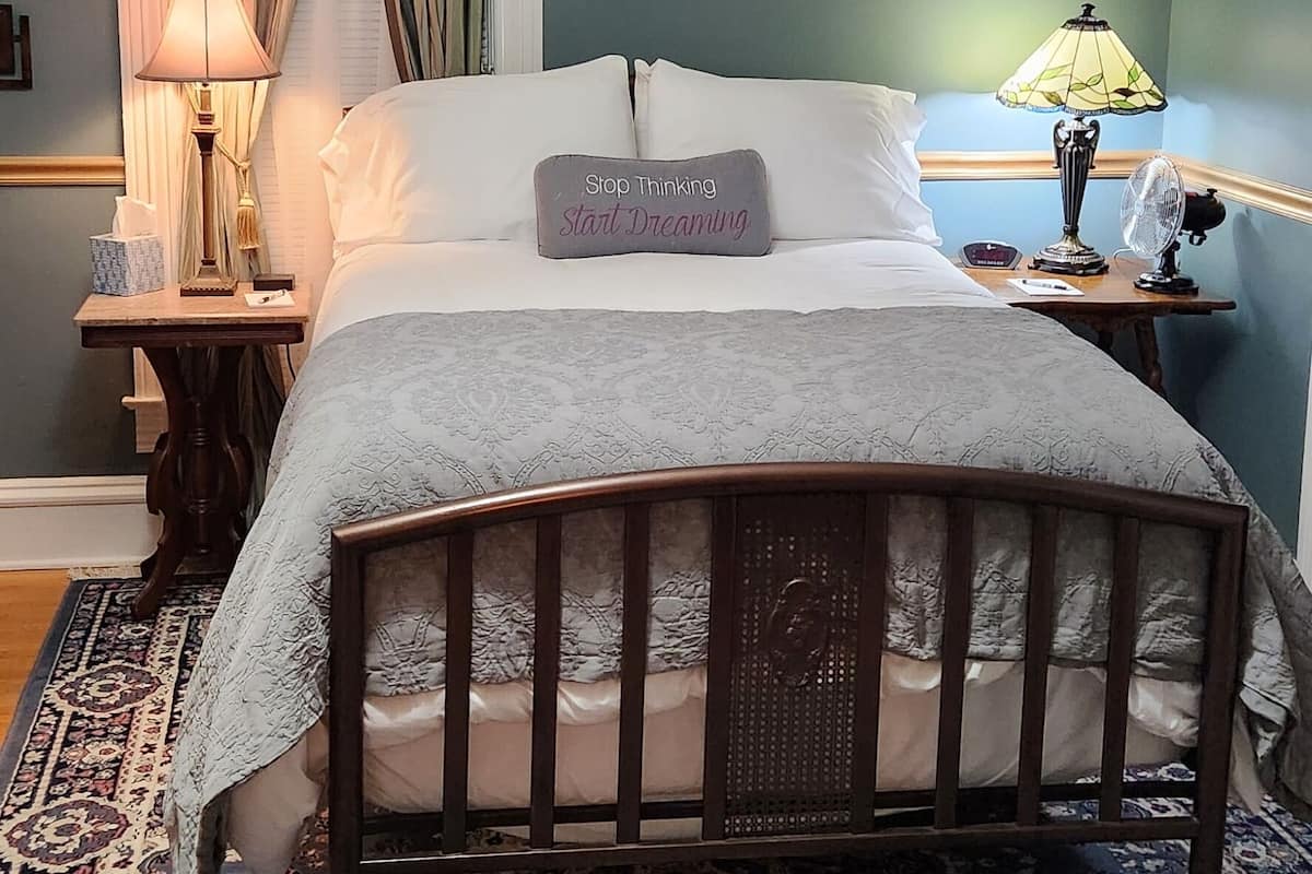A bedroom with a bed, a nightstand, a lamp, a window with curtains, and a hanging light fixture.