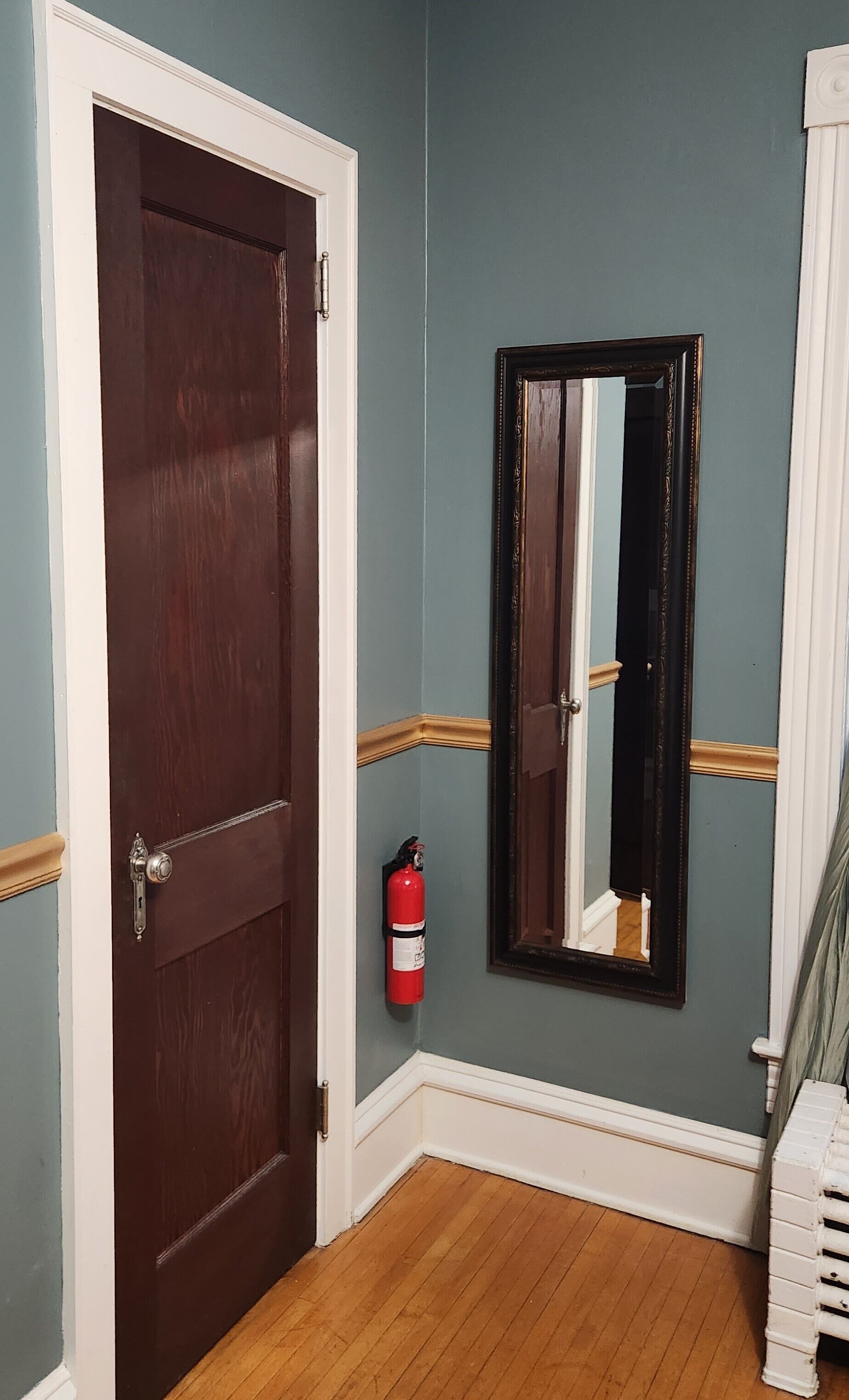 A hallway with a wooden door, a fire extinguisher, and a mirror on the wall.