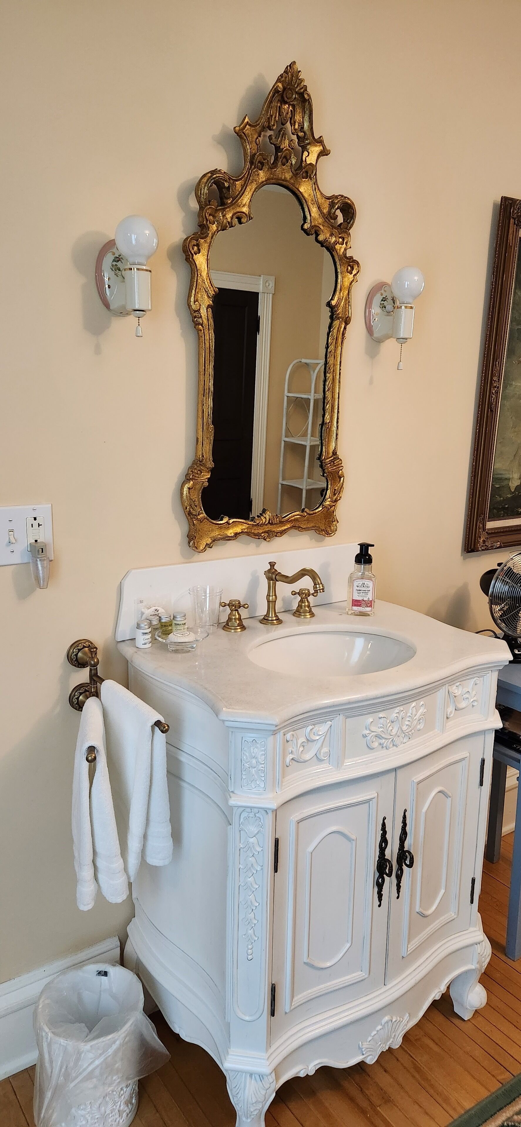 Une salle de bain avec un meuble-lavabo blanc, un miroir à cadre doré et un lavabo blanc.