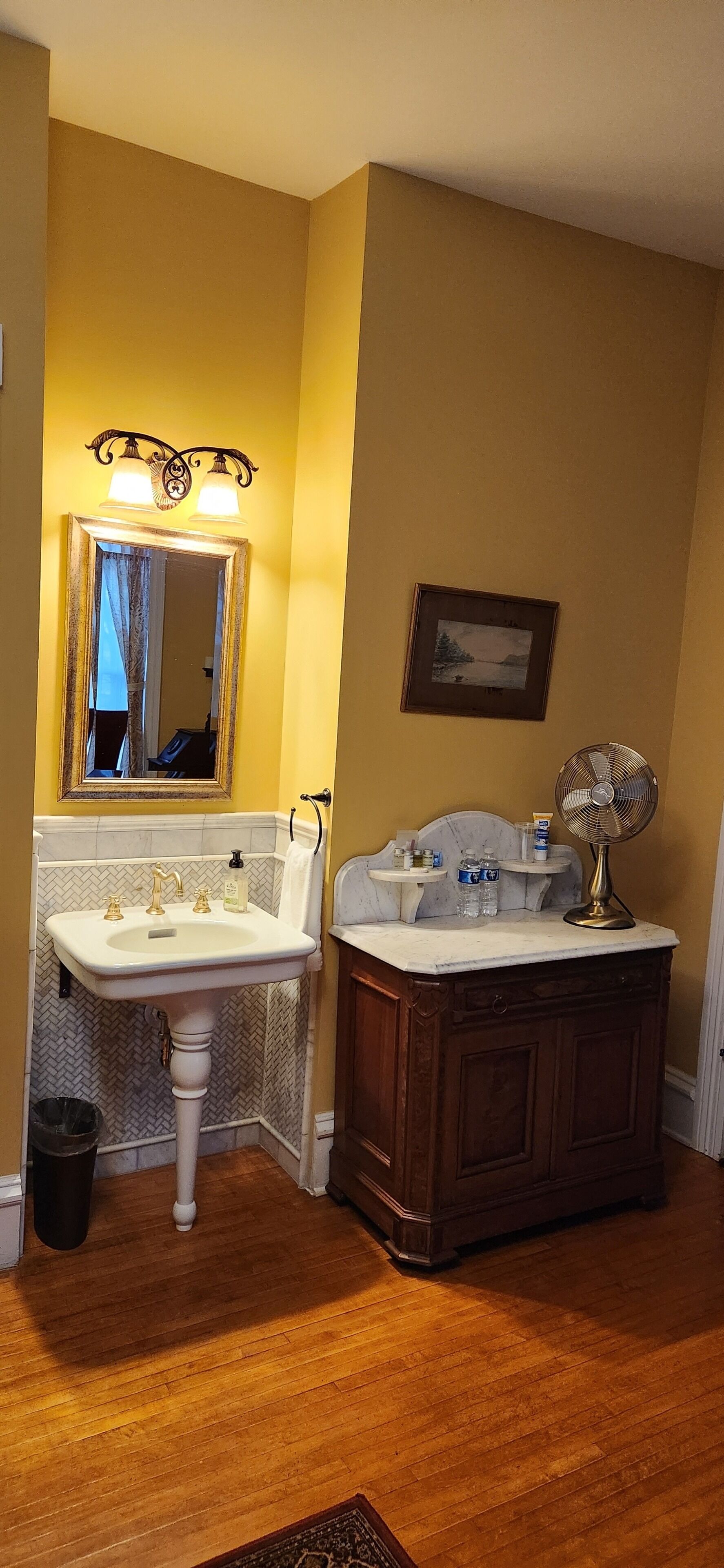 A bathroom with a pedestal sink, vanity, and a wall-mounted fan.