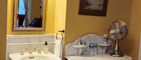 A bathroom with a pedestal sink, vanity, and a wall-mounted fan.
