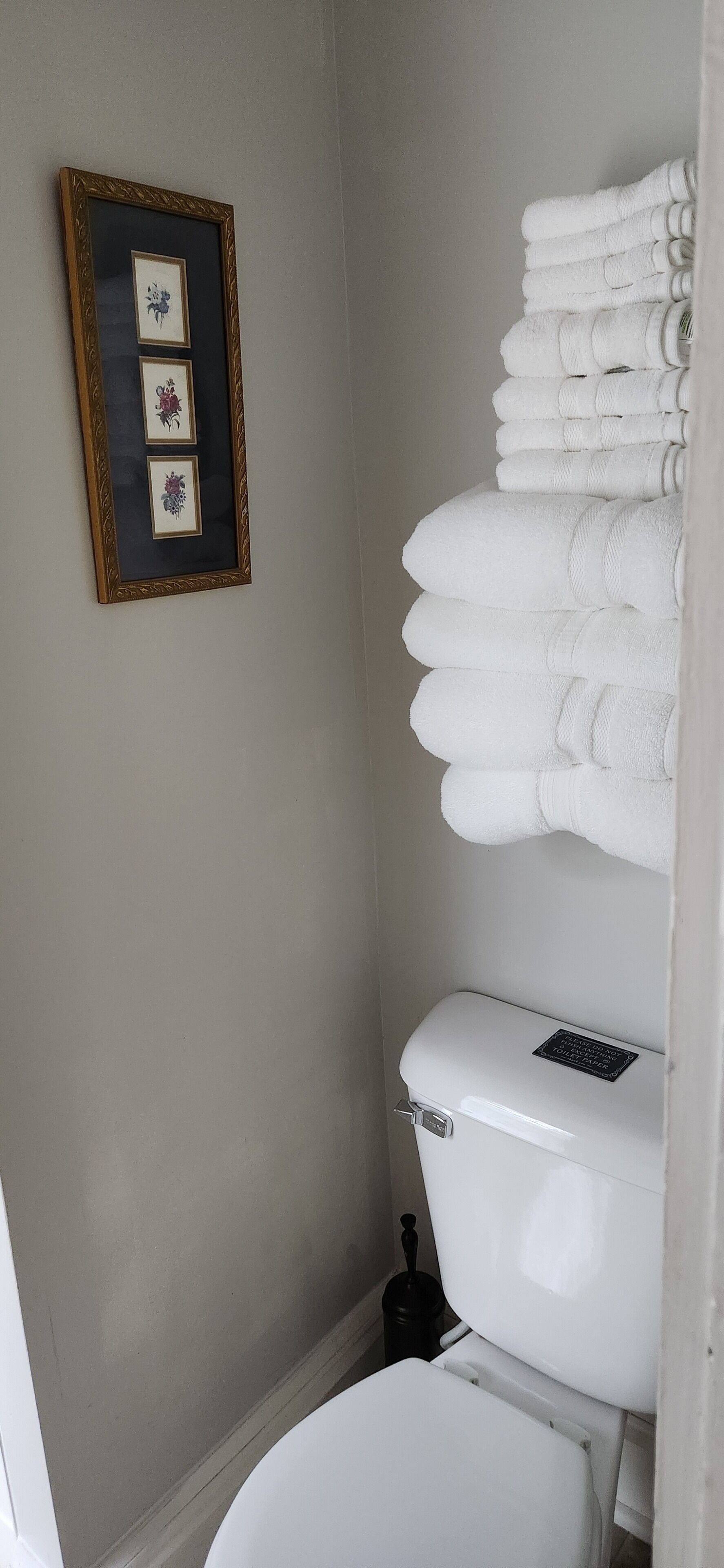 Ein Badezimmer mit Toilette, einem gerahmten Bild an der Wand und einem Stapel weißer Handtücher.