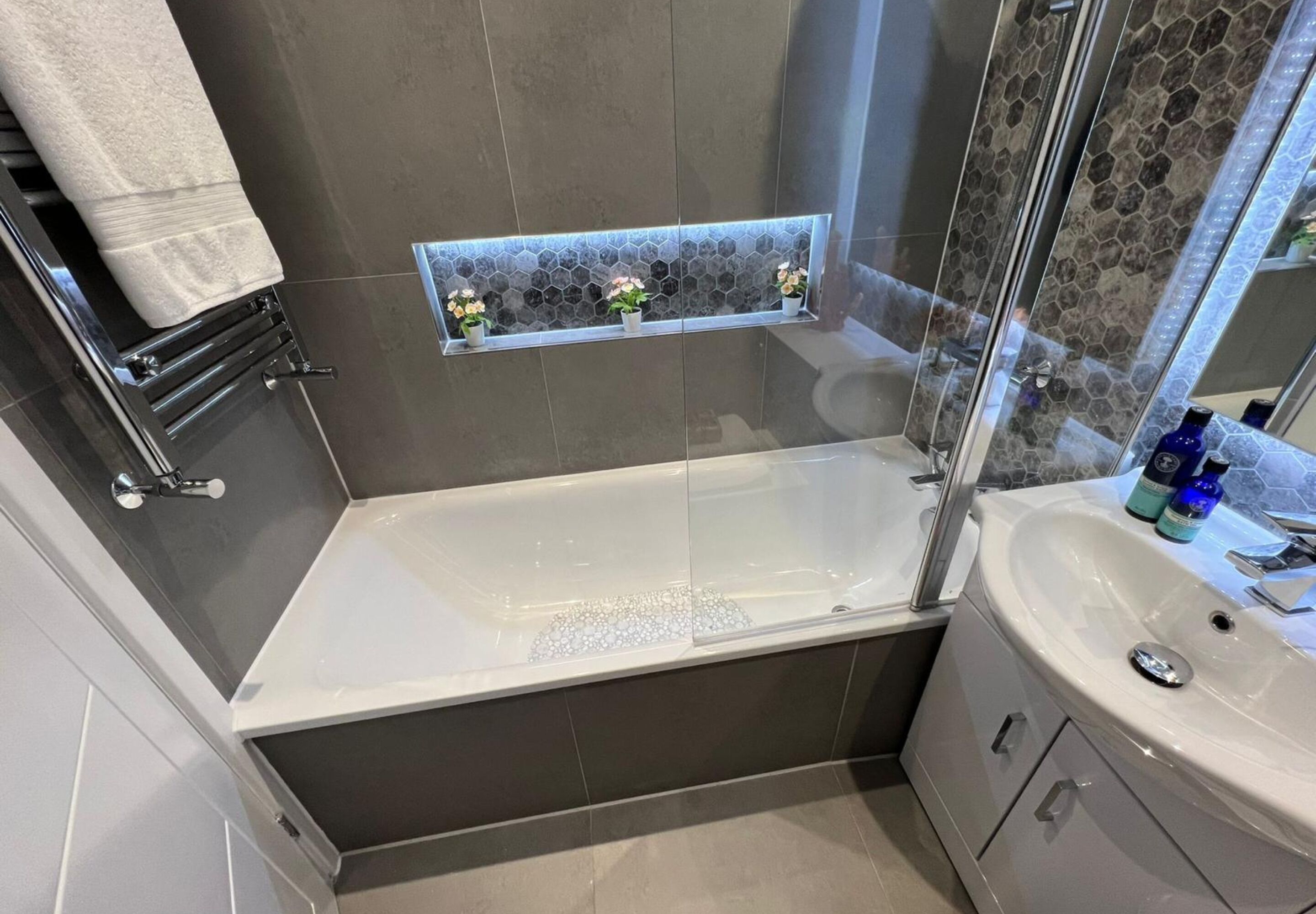 Un baño moderno con bañera, cabina de ducha con paredes de vidrio, tocador con lavamanos y estante con objetos decorativos.
