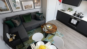 A modern living room with a grey sofa, green and gold cushions, a coffee table with a decorative centerpiece, and a dining area with a round table and chairs. - Stanhope Road Apartments (London)