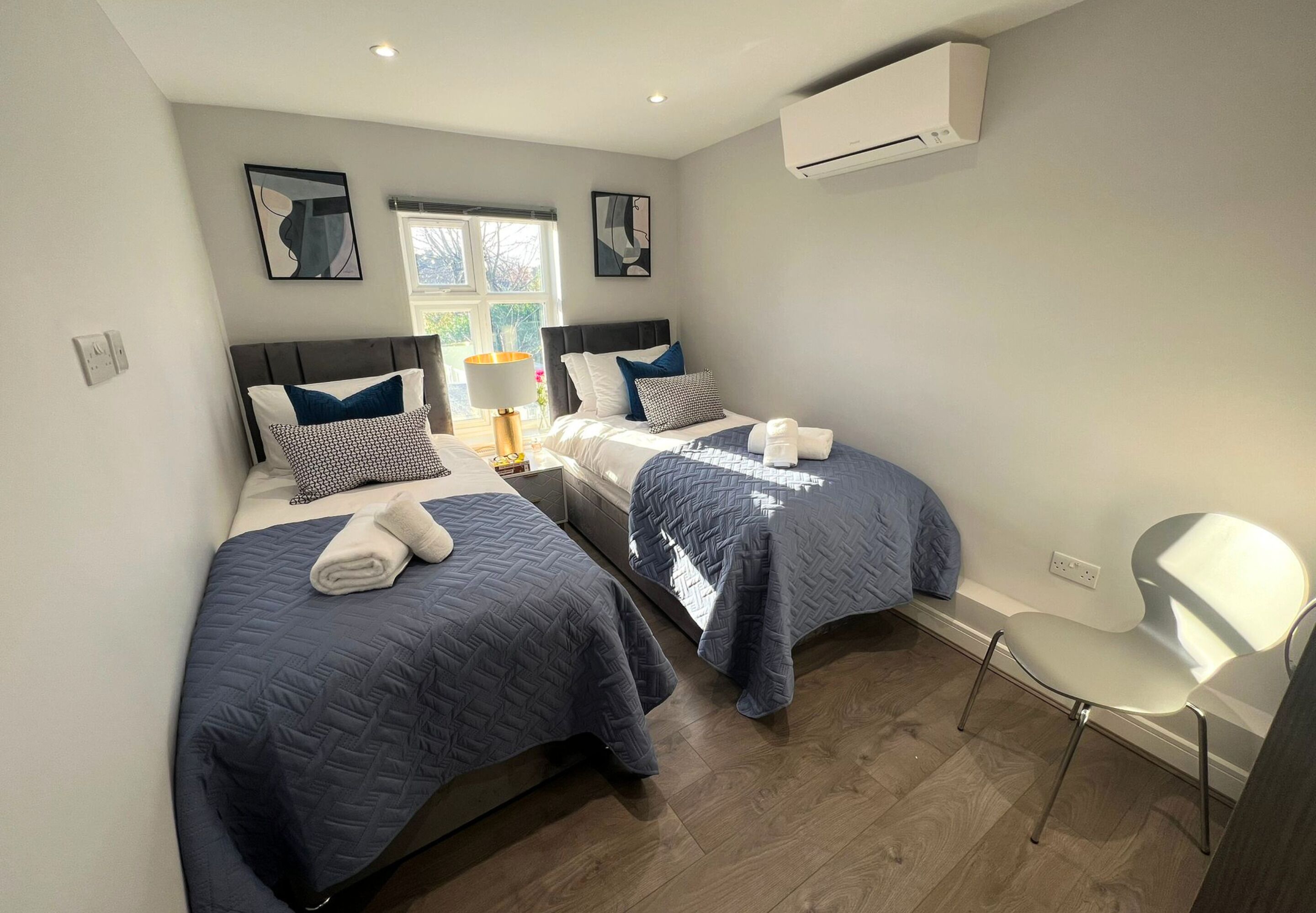 A hotel room with two beds, a chair, and an air conditioning unit.