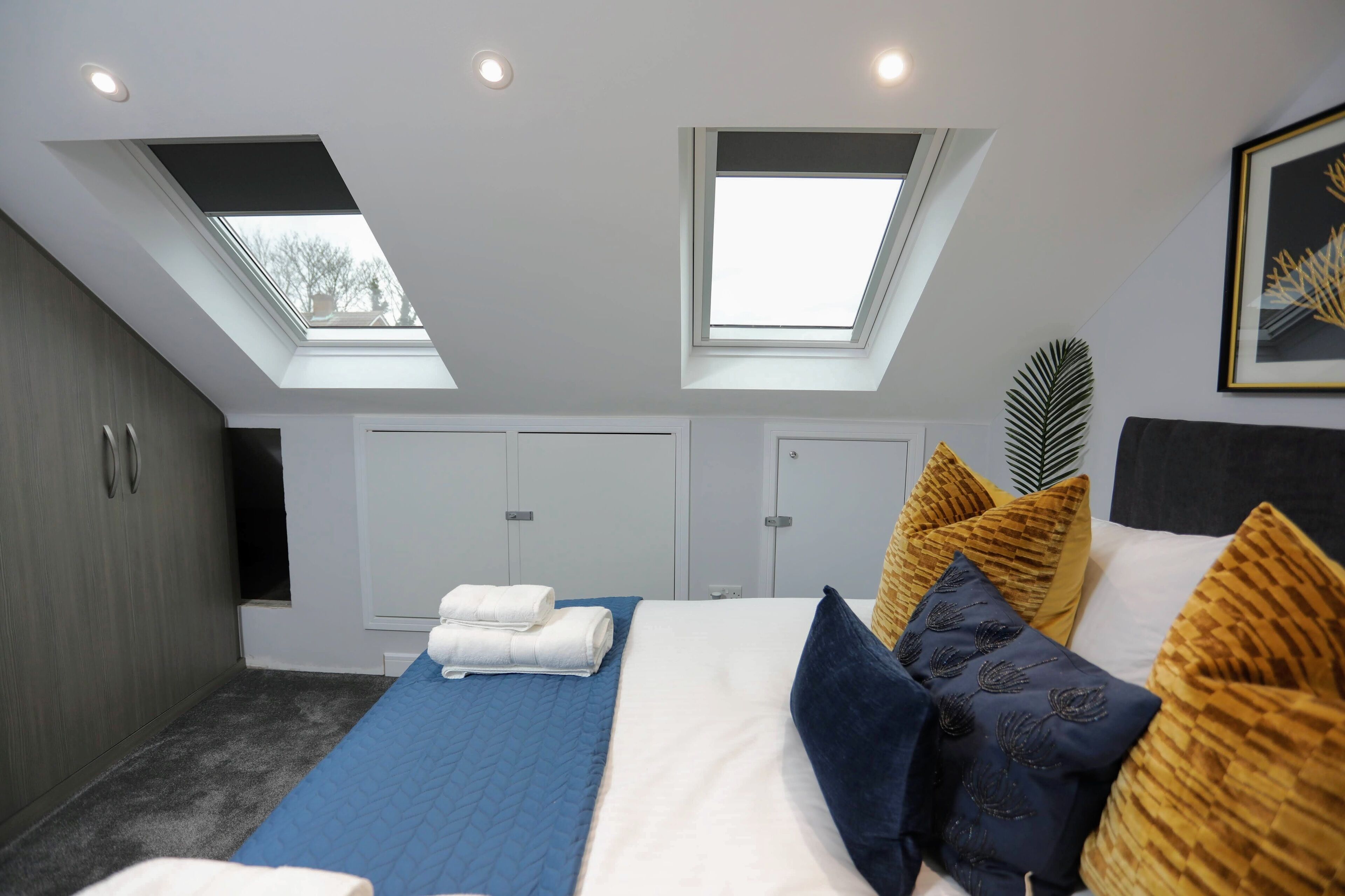 A bedroom with skylights, a bed with blue and white bedding, and a large plant on the wall.