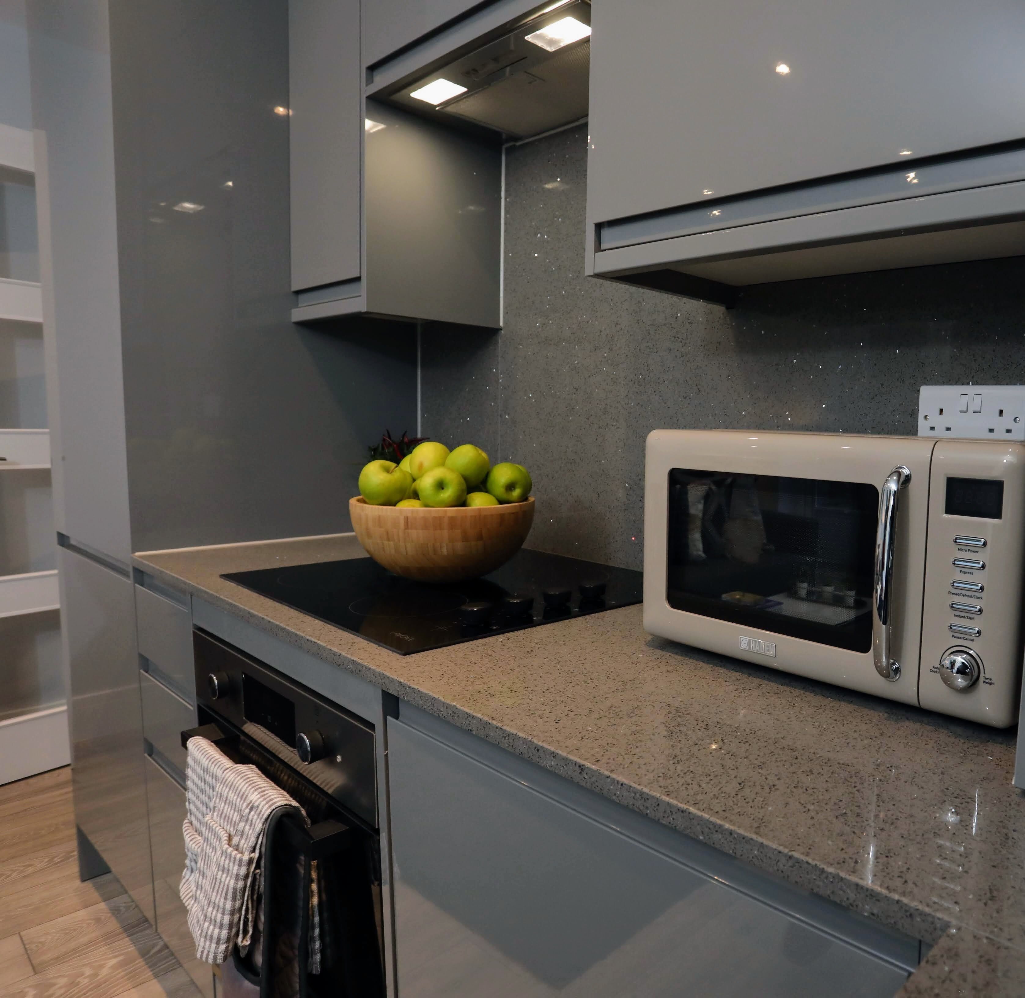 A modern kitchen with a built-in microwave, a wooden bowl of apples on the countertop, and a stainless steel oven.