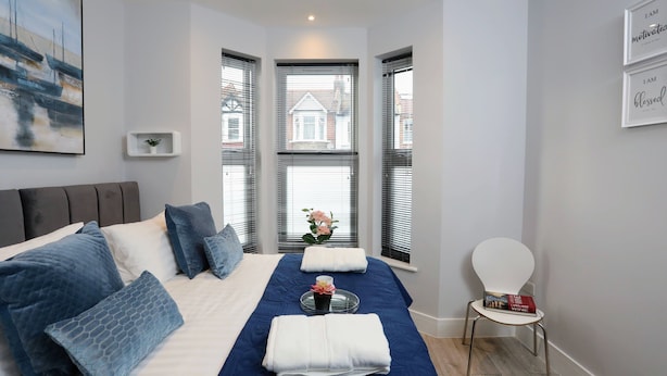 A neatly arranged bedroom with a bed, pillows, a tray with flowers, and a chair. - Stanhope Road Apartments (London)