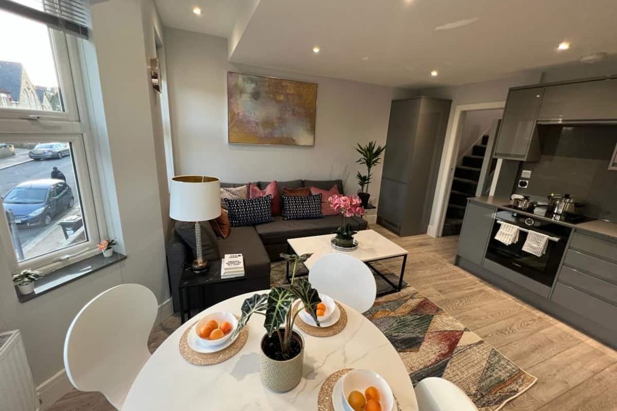 A modern kitchen with a dining area, a sofa, and a large window.